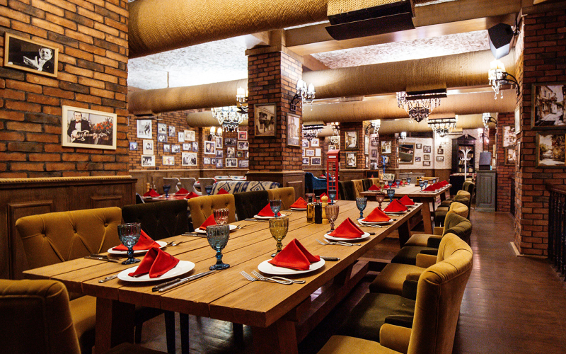 a restaurant hall with red brick walls wooden tables and pipes in the ceiling